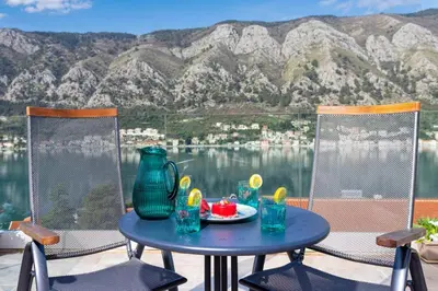 a table with a plate of food on a patio with mountains at De Lux Apartments Sirena in Kotor