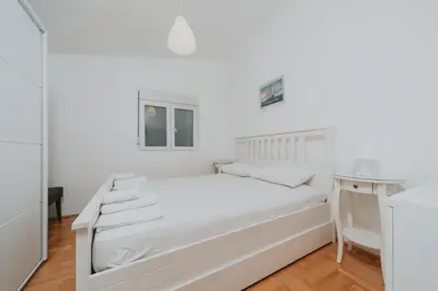 a white bedroom with a white bed and a table at Panoramic Apartment in Budva