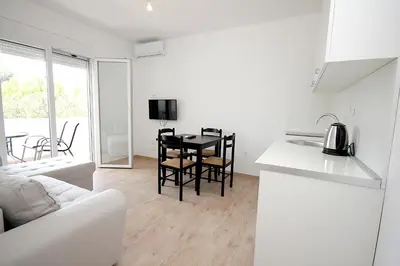 a white kitchen and living room with a table and chairs at Apartmani Begovic in Bar
