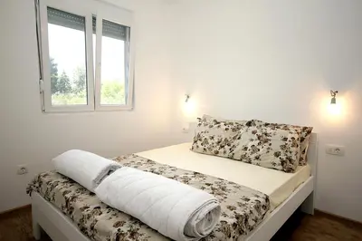 a bedroom with a bed with white walls and a window at Apartmani Begovic in Bar