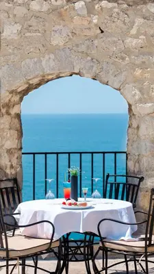 a table with a white table cloth and chairs and the ocean at Kulla e Balshajve in Ulcinj
