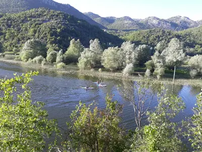two people in boats on a river with mountains at Apartman Sofranac in Rijeka Crnojevića
