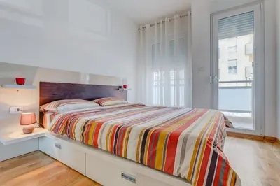 a white bedroom with a bed with a striped comforter at Piano Apartments Delta City in Podgorica