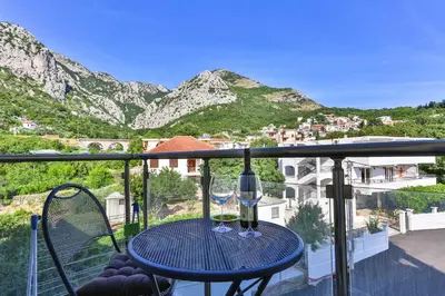 a table with two wine glasses on a balcony with mountains at Luna Apartmani in Sutomore