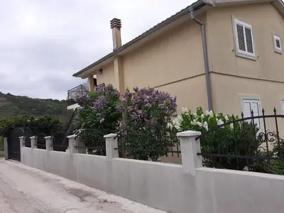 a fence in front of a house with purple and white flowers at Apartment K2 in Radanovići