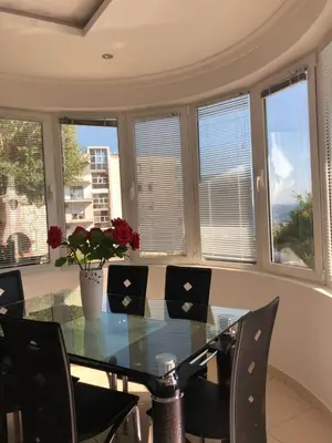a dining room with a glass table and chairs and windows at Apartmani Dini in Ulcinj