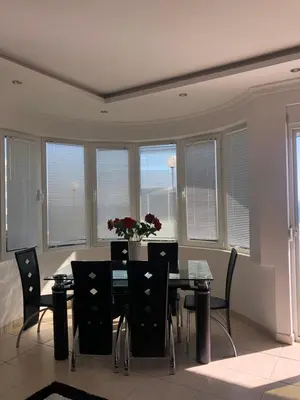 a dining room with a table and chairs and windows at Apartmani Dini in Ulcinj