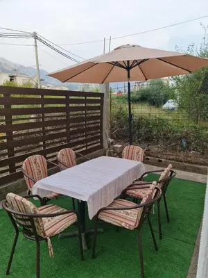 a table and chairs with an umbrella on a lawn at Apartmani Sanja in Bar