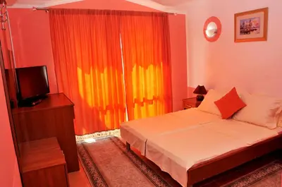 a bedroom with a bed with an orange curtain and a television at Aparthotel Villa Primafila in Ulcinj