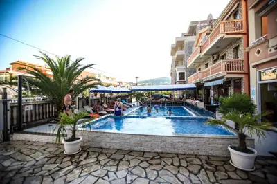 a pool with palm trees and people sitting around it at Aparthotel Villa Primafila in Ulcinj