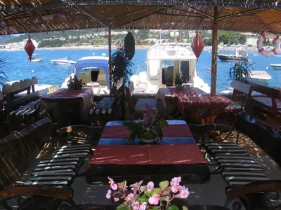 a restaurant with tables and chairs and a boat in the water at Ponta in Rafailovici