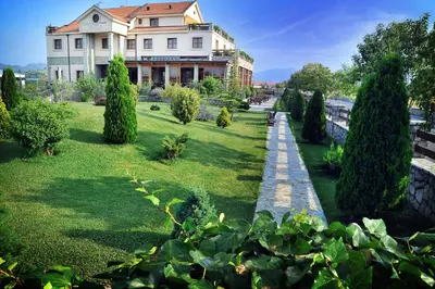 a large house with a lawn with trees and bushes at Hotel Aria in Podgorica