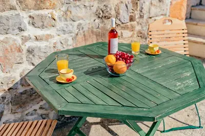 a green table with a bottle of wine and a bowl of fruit at Apartments Bigovo Veljic in Tivat