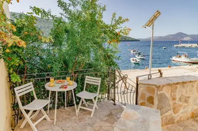 a table and chairs on a balcony with a view of the water at Apartments Bigovo Veljic in Tivat
