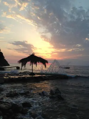 a beach with a straw umbrella and the ocean at Casa Mila apartments & bungalows in Ulcinj