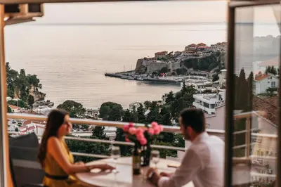 a couple sitting at a table in a restaurant overlooking the water at Apartments Panorama Alaj in Ulcinj