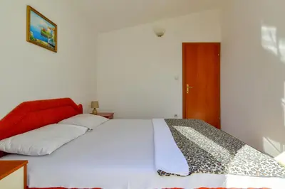 a bedroom with a white bed with a red head board at Rooms and Apartments Oregon in Budva