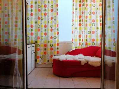 a red ottoman in front of a window with curtains at Apartment White Lily of Budva in Budva