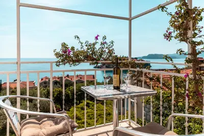 a table and chairs on a balcony with a view of the ocean at Sun Rose Apartments Sveti Stefan in Sveti Stefan