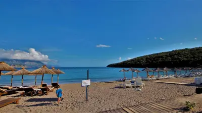 a child standing on a beach with chairs and umbrellas at MM Apartments in Budva