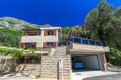 a house with a garage in front of a mountain at Villa Rijeka Rezevici in Petrovac na Moru