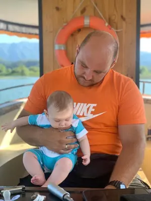a man holding a baby sitting on a boat at Skadar lake Apartments Pajovic in Virpazar
