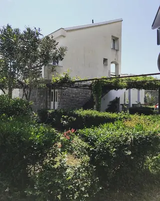 a white building with a brick wall and some bushes at Apartment Dijana in Petrovac na Moru