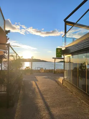 a building with the sun setting over the water at Studio apartman na plaži in Rafailovici