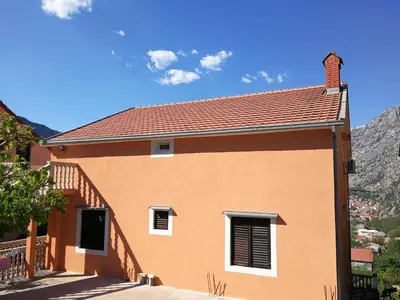 a house with a red roof and mountains in the background at Apartment Misulino in Kotor