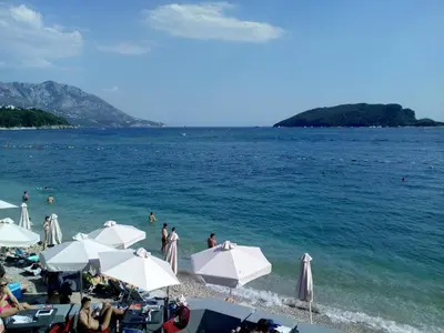 a beach with white umbrellas and people in the water at Red Lux in Budva
