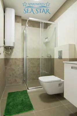 a bathroom with a shower with a toilet and a green rug at Sea Star Apartment in Dobra Voda