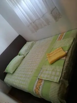 a bed with a green comforter and pillows and a window at Apartment Sara in Podgorica