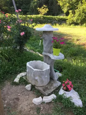 a stone bird bath with a bucket and flowers at Camp Podkraj in Virpazar