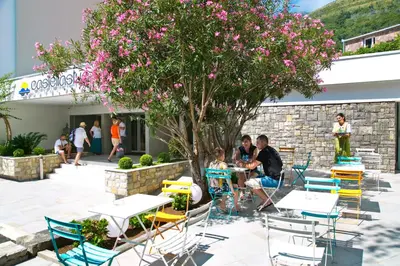a group of people sitting at tables and chairs under a tree at Hotel Castellastva in Petrovac na Moru