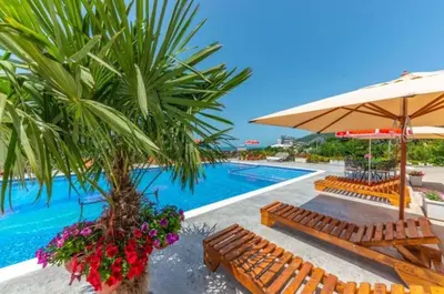 a pool with benches and an umbrella and a palm tree at Apartmani Djurovic in Dobra Voda