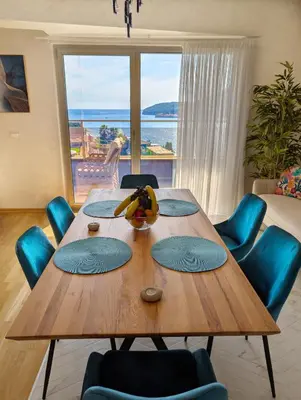 a dining room table with blue chairs and a large window at Lux Apartments Harmonia in Budva