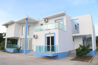 a white house with blue columns and balconies at Gjinaj Apartments in Ulcinj