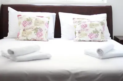 two pillows on a bed with white sheets and pink roses at Ruza apartman in Budva