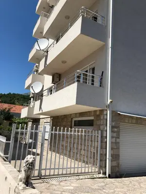 a building with a fence and a dog sitting in front of it at Ruza apartman in Budva