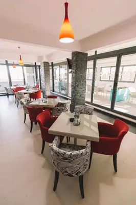 a restaurant with tables and red chairs and windows at Miami apartments in Ulcinj