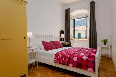 a bedroom with a bed with red pillows and a window at Old Town Clock Tower Apartment in Kotor