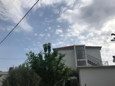 a white house with a tree and a cloudy sky at Apartments Radulović in Ulcinj