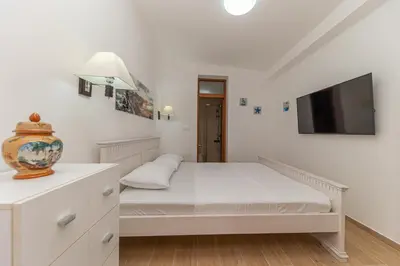 a white bedroom with a bed and a flat screen tv at Vila Dora in Dobra Voda