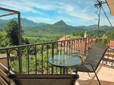 a table and a chair on a balcony with mountains at Village experience - Skadar lake in Virpazar