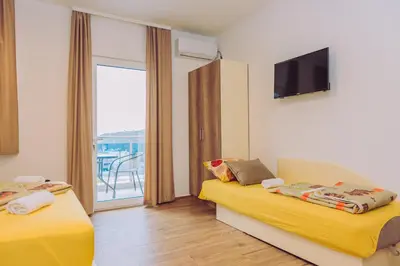 a room with two beds and a tv and a balcony at Apartments Krstovic in Sutomore