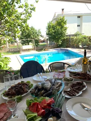 a table topped with plates of food next to a pool at Andolly Apartments in Bar
