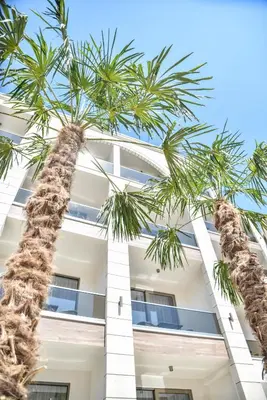 a tall white building with palm trees in front of it at Hotel Prova in Ulcinj