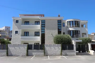 a white building with a fence in front of it at Apartmani Nilaj in Ulcinj
