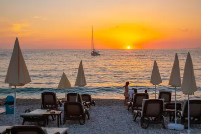 a beach with chairs and umbrellas at sunset at Apartments Oliva in Utjeha