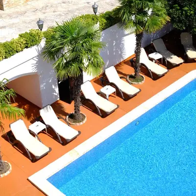 a row of lounge chairs and palm trees next to a pool at Hotel Kleopatra in Ulcinj